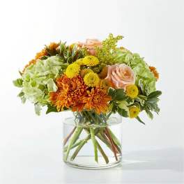 Orange and yellow flowers arranged in a clear glass vase with pale green blooms