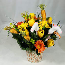 Yellow and orange floral arrangement in a carrot-patterned pot with plush bunny ears