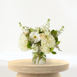 White floral arrangement in a clear glass vase on a wooden table
