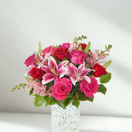 Pink and red roses with lilies in a speckled white vase