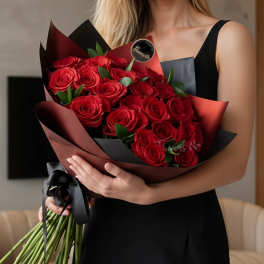 Woman holding a bouquet of red roses wrapped in dark paper