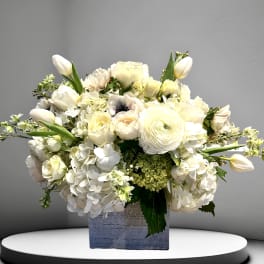 White floral arrangement in a square vase with tulips and roses
