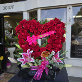 Heart-shaped red rose arrangement with lilies and pink ribbons