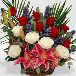 Basket arrangement of red and white roses with pink lilies and purple flowers.