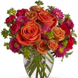 Arrangement of orange roses and bright pink mums in a clear glass vase