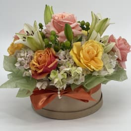 Mixed roses and lilies arranged in a round gift box with an orange ribbon