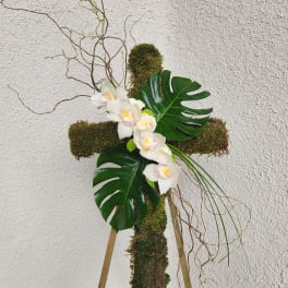Moss-covered cross arrangement with white orchids and large tropical leaves