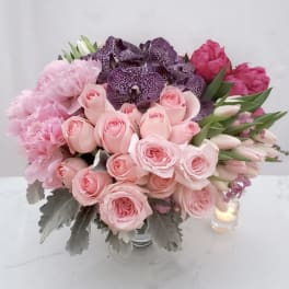 Pink and purple bouquet of roses, tulips, and orchids in a glass vase