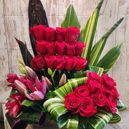 Red roses and pink lilies arranged in a wooden box with striped leaves