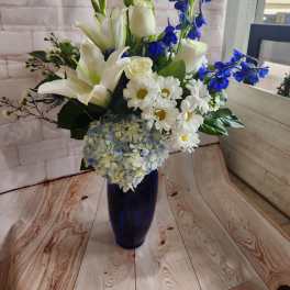 White lilies, roses, daisies, and blue flowers in a dark blue vase