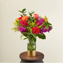Tall mixed bouquet of bright flowers in a clear vase with a gold base