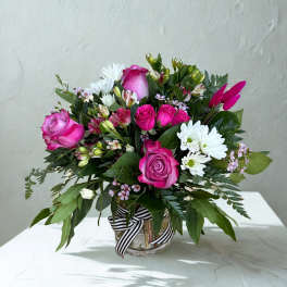 Pink roses and white daisies in a glass vase with a striped ribbon