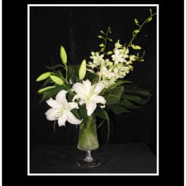 White lilies and orchids arranged in a glass vase
