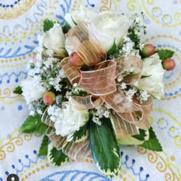 Compact white rose corsage with peach ribbon, white filler flowers, and berries on variegated foliage.
