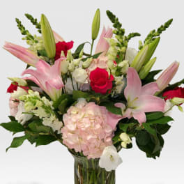 Tall arrangement of pink lilies, red roses, and white flowers in a clear glass vase