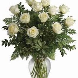 White roses in a clear glass vase with greenery