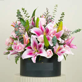 Pink lilies and roses arranged in a black box container