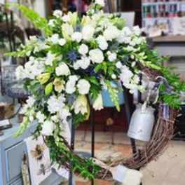 Large white floral wreath with trailing greenery and a silver watering can