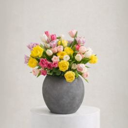 Mixed bouquet of pink, yellow, and white flowers in a gray vase