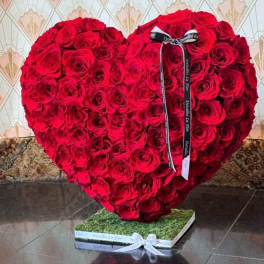 Heart-shaped arrangement of red roses with a ribbon on a square base