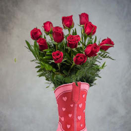 Red roses arranged in a pink cowboy boot vase with heart accents