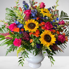Colorful bouquet with sunflowers, pink roses, and blue flowers in a white vase