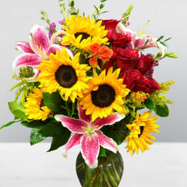 Bouquet of sunflowers, red roses, and pink lilies in a glass vase