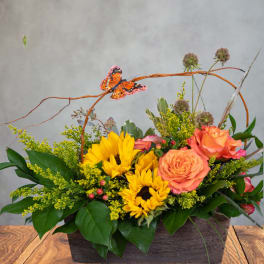Sunflowers and orange roses in a rectangular wooden container with a butterfly accent