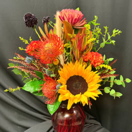 Bright mixed bouquet with a sunflower in a red glass vase