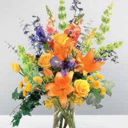 Mixed bouquet of orange, yellow, and purple flowers in a clear glass vase