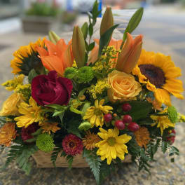Mixed bouquet with sunflowers, roses, lilies, and daisies in a basket