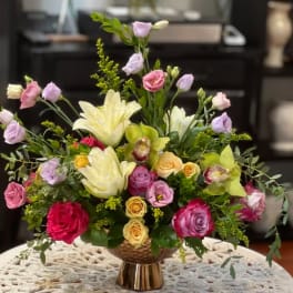 Mixed bouquet of roses, lilies, and lisianthus in a gold vase