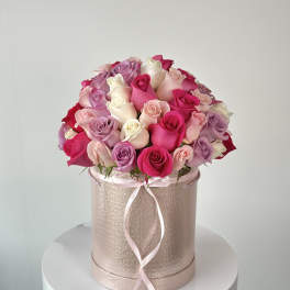 Pink and lavender roses arranged in a round hatbox with a ribbon