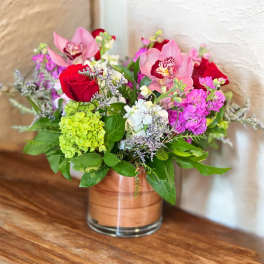 Arrangement of pink orchids, red roses, green hydrangea, and mixed blooms in a clear glass vase