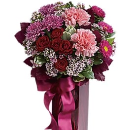 Bouquet of pink and red flowers in a tall magenta vase with ribbon