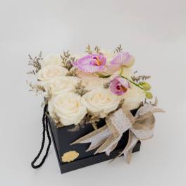 White roses and pink orchids in a black gift box with a ribbon bow