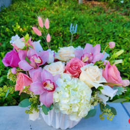 Pink and white floral arrangement in a white vase with orchids and roses