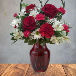 Red roses and white daisies arranged in a red glass vase