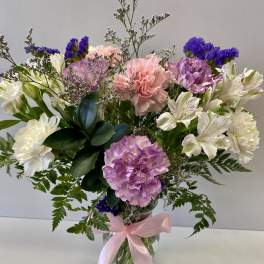 Bouquet of pink, purple, and white flowers in a glass vase with a pink ribbon