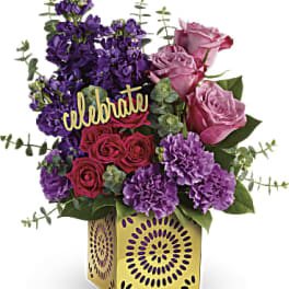 Purple and pink flower arrangement in a decorative gold vase with a "celebrate" sign