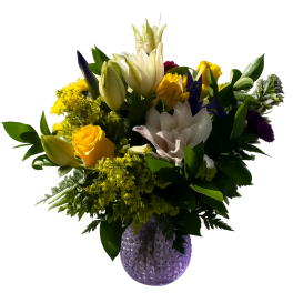 Mixed bouquet of yellow, white, and purple flowers in a textured vase