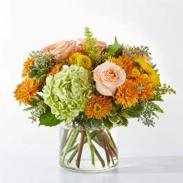 Bouquet of peach roses, green hydrangea, and orange mums in a glass vase