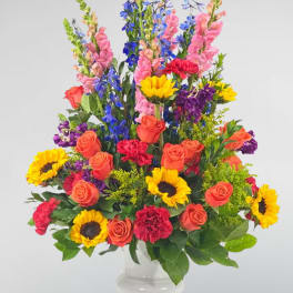 Colorful mixed bouquet in a clear glass vase with roses, sunflowers, and tall blue blooms