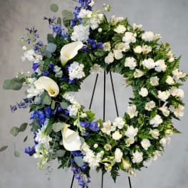Large floral wreath with white calla lilies and blue flowers on a stand
