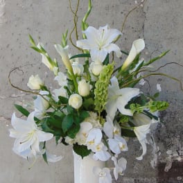 Tall white arrangement with lilies, calla lilies, roses, and orchids in a white vase