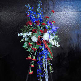 Standing spray of red roses and carnations with blue delphinium and white flowers on an easel