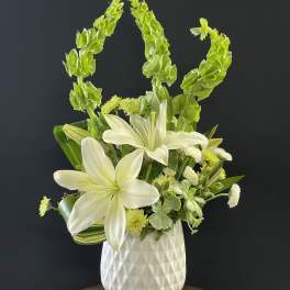 White lilies and green blooms in a white vase