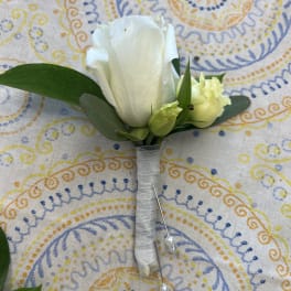 White rose boutonniere with small buds and greenery wrapped in white ribbon with pearl pins on patterned cloth