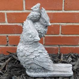 Three gray bird statues on mulch in front of a brick wall