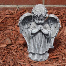 Stone angel statue with folded hands in a mulch bed